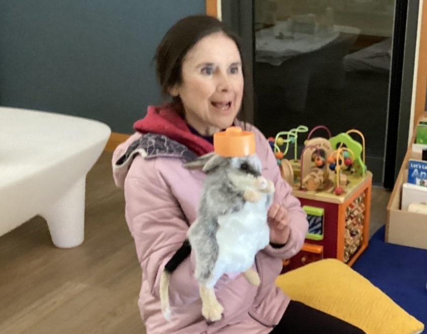Dr Olivia Karaolis with puppet, Joy, who is a Bilby. Olivia and Joy are sitting on the floor in an early childhood centre engaging with children (the children are not in the photo).